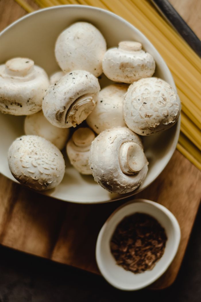 Crafting Captivating Headlines: Your awesome post title goes here Top view of fresh white mushrooms in a bowl with pasta and spices on a wooden board.